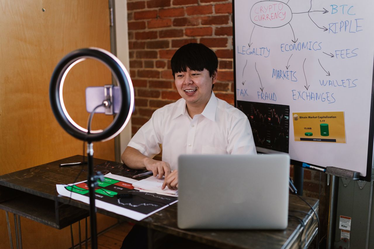 about-01 Man discussing cryptocurrency economics with ring light and laptop, engaging content creation.